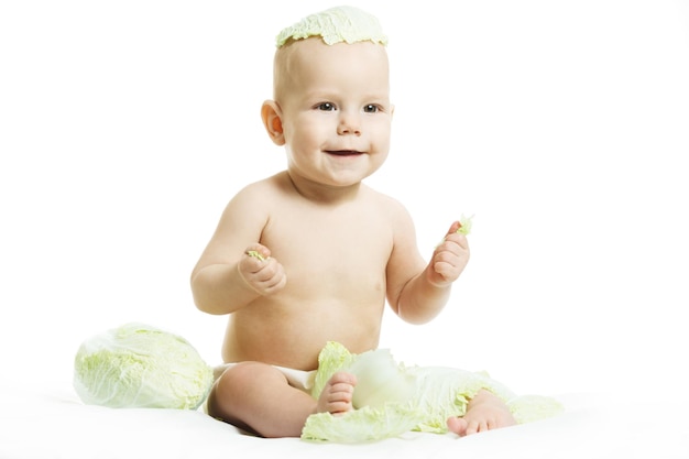 Bebê nu na fralda está brincando com frutas e legumes orgânicos frescos isolados em um fundo branco Criança mordendo uma cabeça verde fresca de repolho Comida saudável para o conceito de crianças