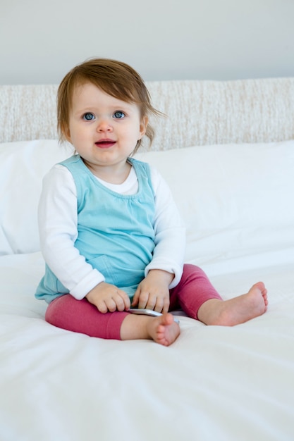 Bebé de ojos azules sonriendo, sentado en la cama