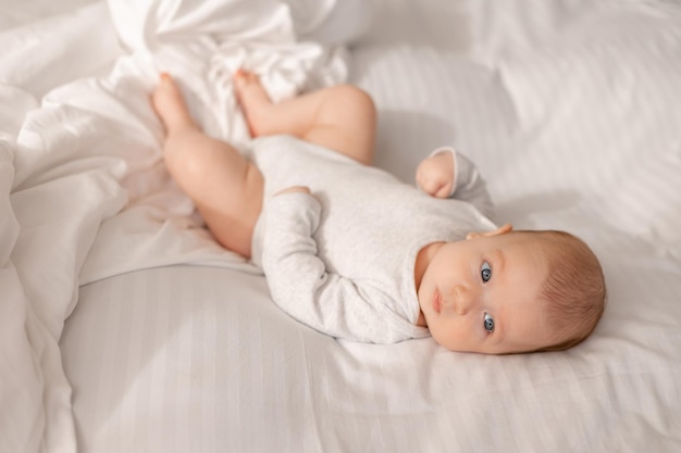 Bebé con ojos azules en un traje blanco está acostado en una vista superior de la cama blanca