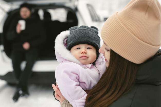 Bebê olha para a câmera e sorri nos braços de sua mãe na floresta coberta de neve de inverno