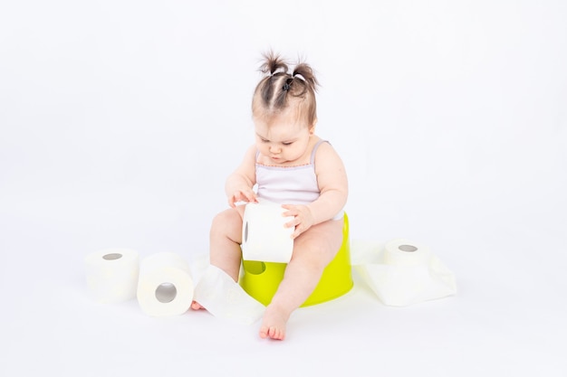 Bebé en un orinal verde con papel higiénico sobre blanco