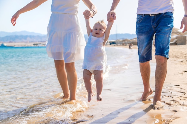 Bebé y padre madre están caminando por la playa.