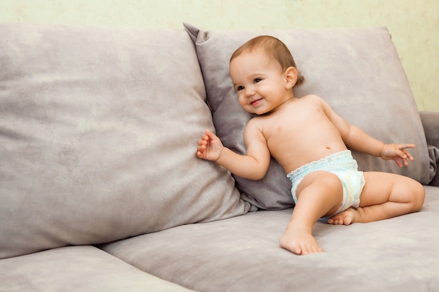 Bebé en pañal gatea en el sofá. el bebé tiene 11 meses.