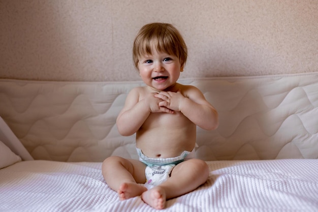 Un bebé en pañales sonríe sentado en una cama.