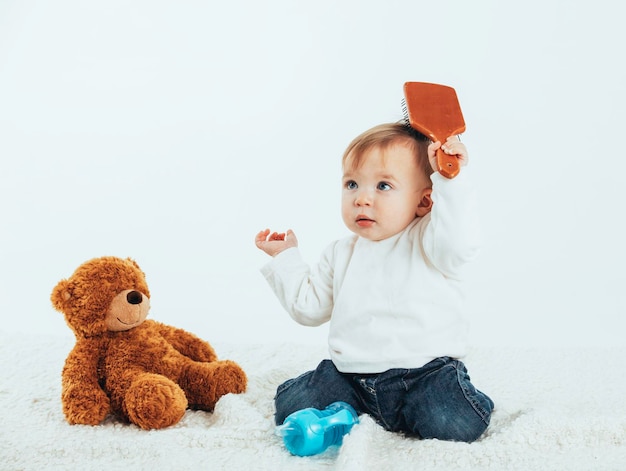 Bebê penteando o cabelo com um ursinho de pelúcia ao seu lado