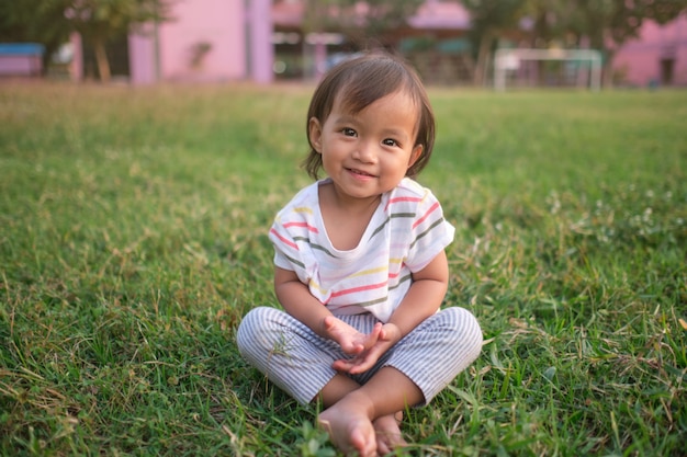 Bebé pequeno e fofo asiático de 1 a 2 anos de idade, menina, sorrindo para a câmera, praticando ioga descalça e meditando ao ar livre