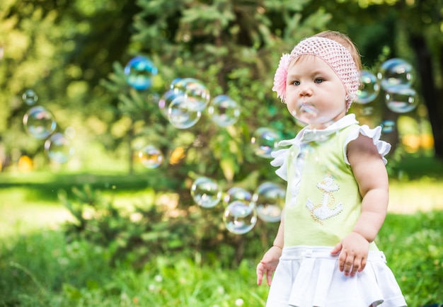 Bebé pequeno no vestido verde que está e que olha bolhas no ar