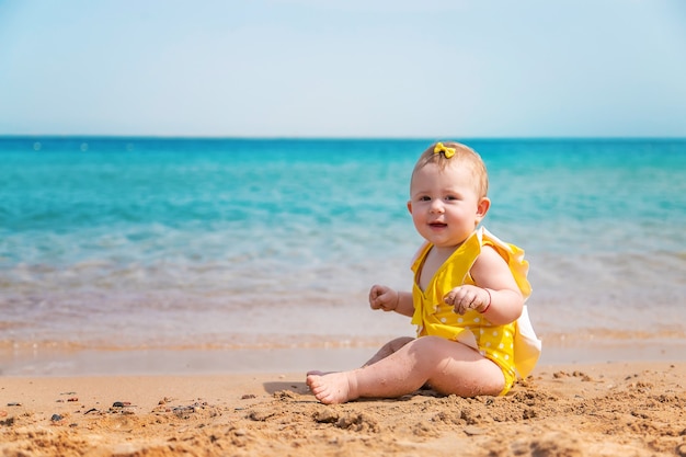 Bebé en la playa cerca del mar con chaleco amarillo