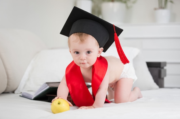 Bebé prodigio en gorra de graduación alcanzando la manzana