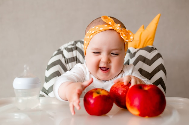 Bebê que come frutas trituradas que sentam-se no fim da cadeira. olhando para a câmera. estilo de vida saudável. infância.