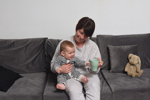 El bebé que está con la madre en el sofá y quiere tomar la taza.