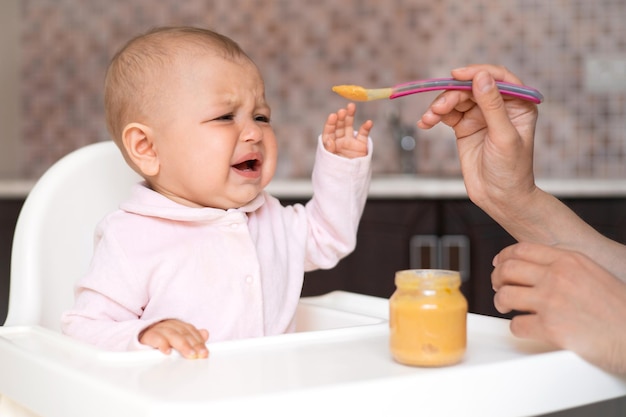 Un bebé que llora se niega a comer Comida para bebés Un niño malhumorado la verdadera maternidad Alimentar al bebé con una cuchara Puré de verduras y frutas Cocina