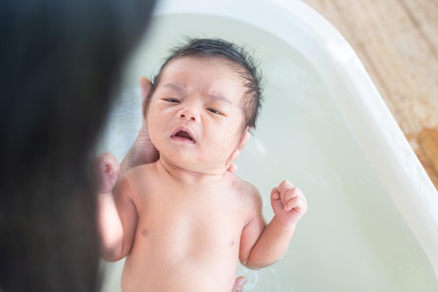 Foto bebê recém-nascido asiático lavando o corpo em uma banheira chuveiro de mãe e limpando seu bebêconceito de cuidados com a saúde do recém-nascidoensaio de estilo de vida com luz natural e profundidade de campo rasa