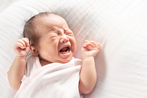 Bebê recém-nascido bonitinho chorando deitado na cama.