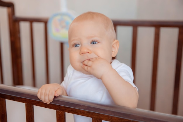 Bebê recém-nascido bonitinho está sentado em um berço menino está sentado no berço sorrindo