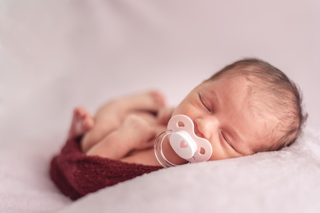 Bebê recém-nascido com chupeta dobrada em uma bola de lã