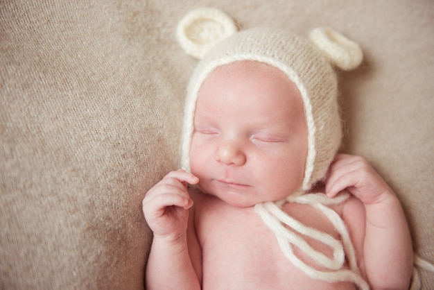 Bebê recém-nascido dorme na cama com um chapéu branco com orelhas