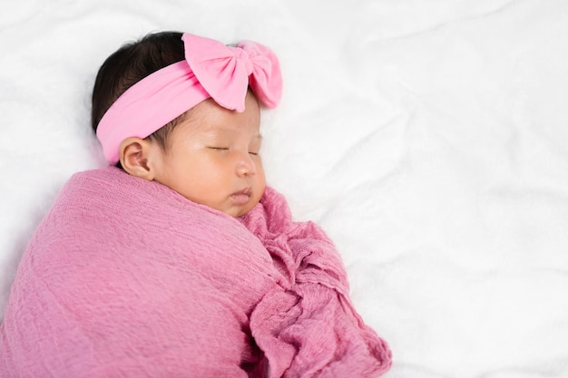 Bebê recém-nascido dormindo em um cobertor de pano rosa em uma cama