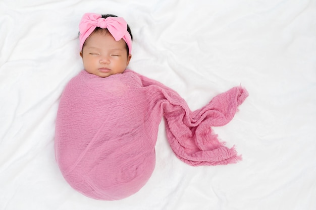 Bebê recém-nascido dormindo em um cobertor de pano rosa em uma cama