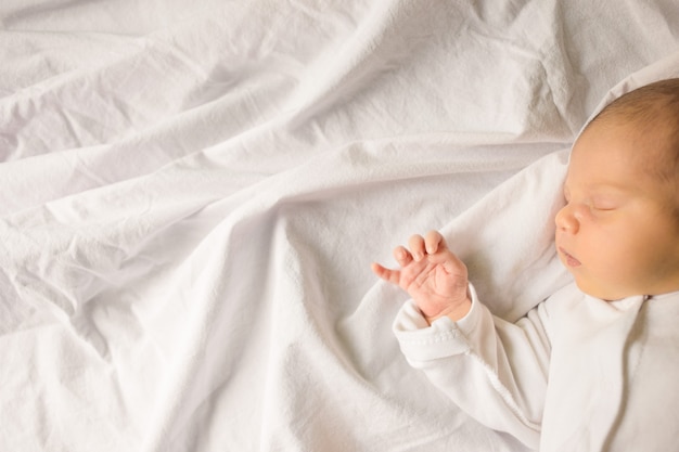 Bebê recém-nascido dormindo enrolado em um cobertor branco