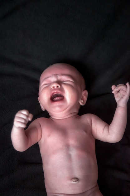 Foto bebê recém-nascido em fundo escuro mostra suas emoções. retrato de bebê de um mês com olhos azuis no trocador na sala. close-up de uma criança linda em fundo preto. conceito de nova vida