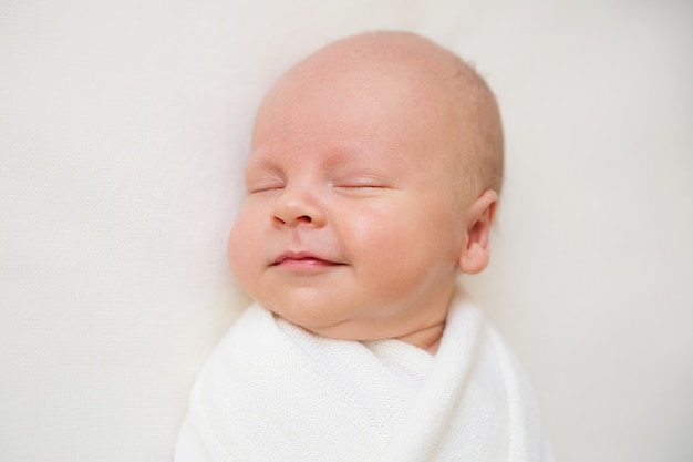 Bebé recém-nascido em um fundo branco. Sorrisos de bebê. Menino está dormindo. Envoltório do bebê branco