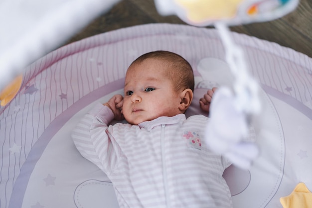 Bebê recém-nascido fofo deitado em um tapete em desenvolvimento Rosto emocional Maternidade Criança doce brincando com brinquedos no tapete Estilo de vida