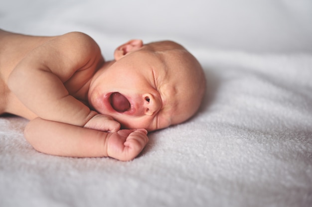 Bebé recém-nascido recém-nascido bocejando menino dormindo no berço. Criança saudável, conceito de hospital e maternidade feliz. Berçário.