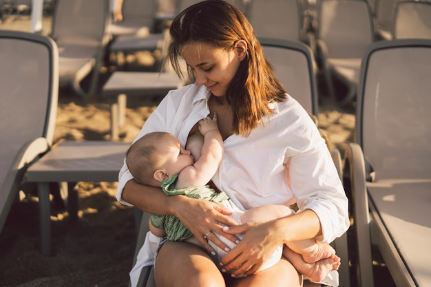 Foto bebê recém-nascido sugando leite do seio da mãe na praia