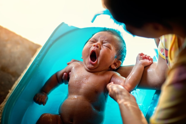 Bebé recién nacido asiático bañándose en las manos de las madres con boquiabierto