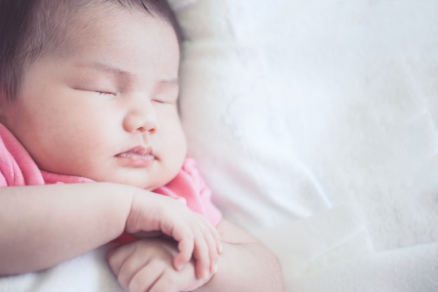 Bebé recién nacido asiático durmiendo en la cama blanca