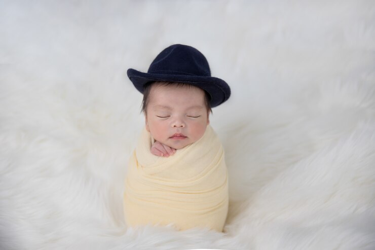 Bebé recién nacido asiático con un sombrero en amarillo swaddle dormir sobre una alfombra mullida blanca