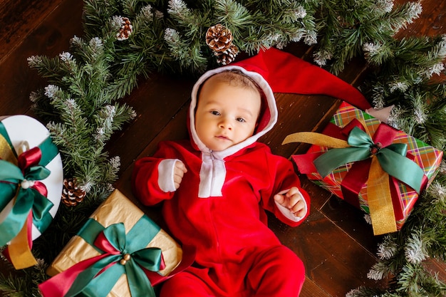 Bebé recién nacido disfrazado de Santa Claus se encuentra en medio de una corona de árboles de Navidad