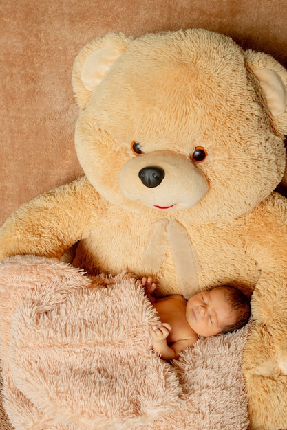 Foto bebé recién nacido de dos semanas durmiendo en un oso de peluche.