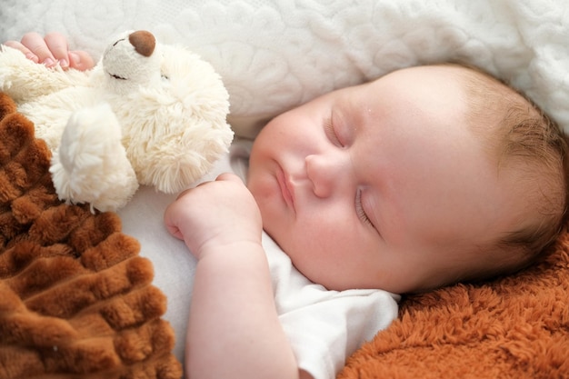 Un bebé recién nacido duerme en una cama Un oso de peluche yace cerca de la madre y el niño