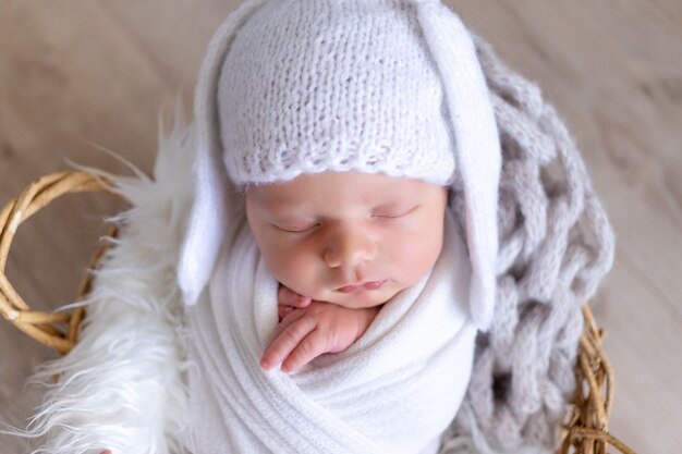 Un bebé recién nacido duerme dulcemente en un capullo de pañal en un sombrero con orejas de liebre, Retrato