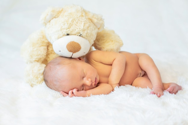 Un bebé recién nacido duerme con un osito de peluche.