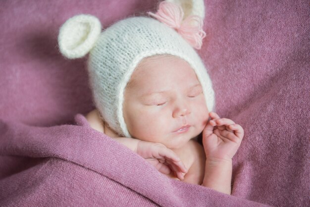 Un bebé recién nacido duerme con un sombrero con orejas sobre una manta rosa