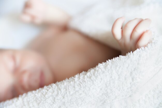 Bebé recién nacido durmiendo cubierto con manta blanca. De cerca