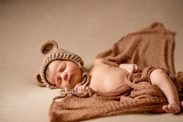 Bebé recién nacido durmiendo en gorro de punto se encuentra en tela marrón