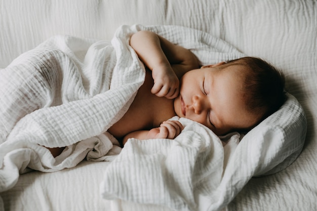 Bebé recién nacido durmiendo en un nido cubierto con una manta de muselina blanca
