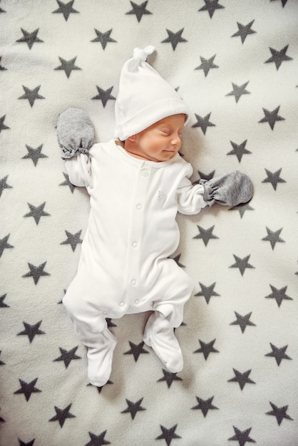 Bebé recién nacido durmiendo en ropa y un sombrero blanco a cuadros con estrellas | Foto Premium
