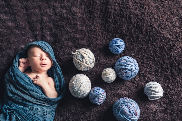 Bebé recién nacido envuelto en tela azul se encuentra en la cama con bobinas de hilos.