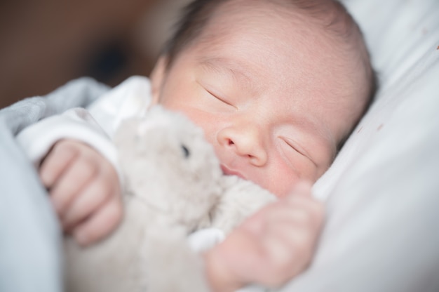 Foto bebé recién nacido que duerme en cama con el pequeño conejo. concepto de la familia y del amor. niño asiático.