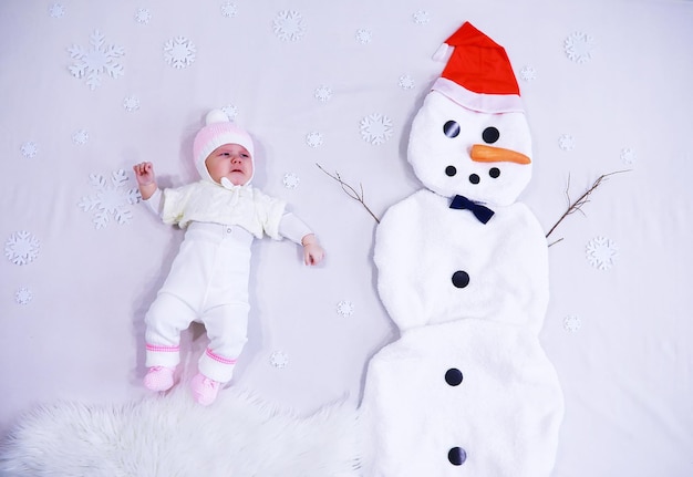 Bebé recién nacido sobre un fondo blanco. Pintura de tela blanca. Muñeco de nieve y bebé. Vacaciones navideñas.
