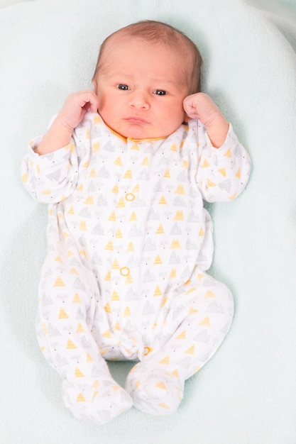 Bebé recién nacido sonriente de longitud completa acostado en la cama con las manos en la cabeza de los dedos