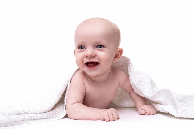 Un bebé recién nacido con una sonrisa en la cara se asoma por debajo de una toalla sobre un fondo blanco.