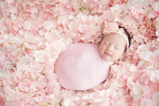 El bebé recién nacido tiene un dulce sueño con una sonrisa con una diadema rosa y envuelto con una envoltura rosa durmiendo en muchas hortensias rosadas como un campo de flores Disparo en la parte superior y el fondo gradualmente borroso