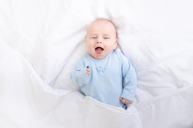 Bebé riendo en la cama debajo de la manta bebé de sueño saludable