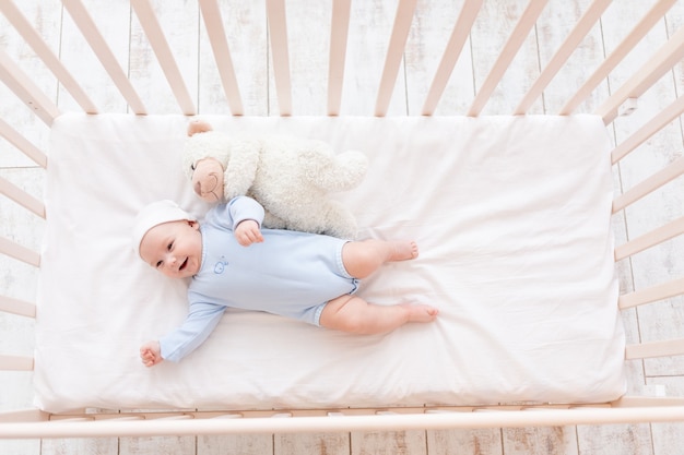 Bebê rindo no berço, bebê fofo de 3 meses com ursinho de pelúcia, crianças e conceito de nascimento